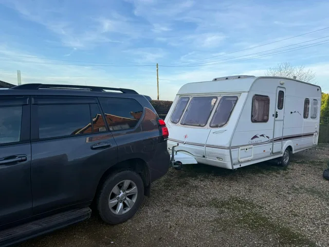 Caravan beside a tow vehicle on a grass and gravel pitch